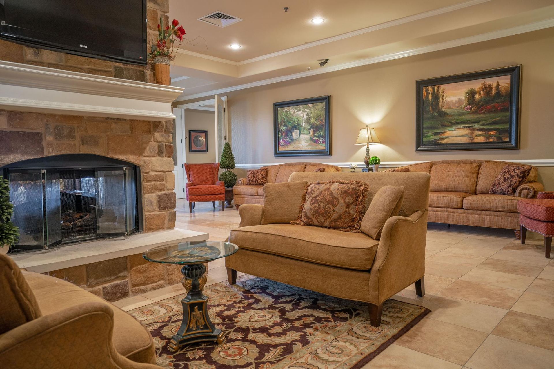 Cozy living room with fireplace, couches, paintings, and a patterned rug.
