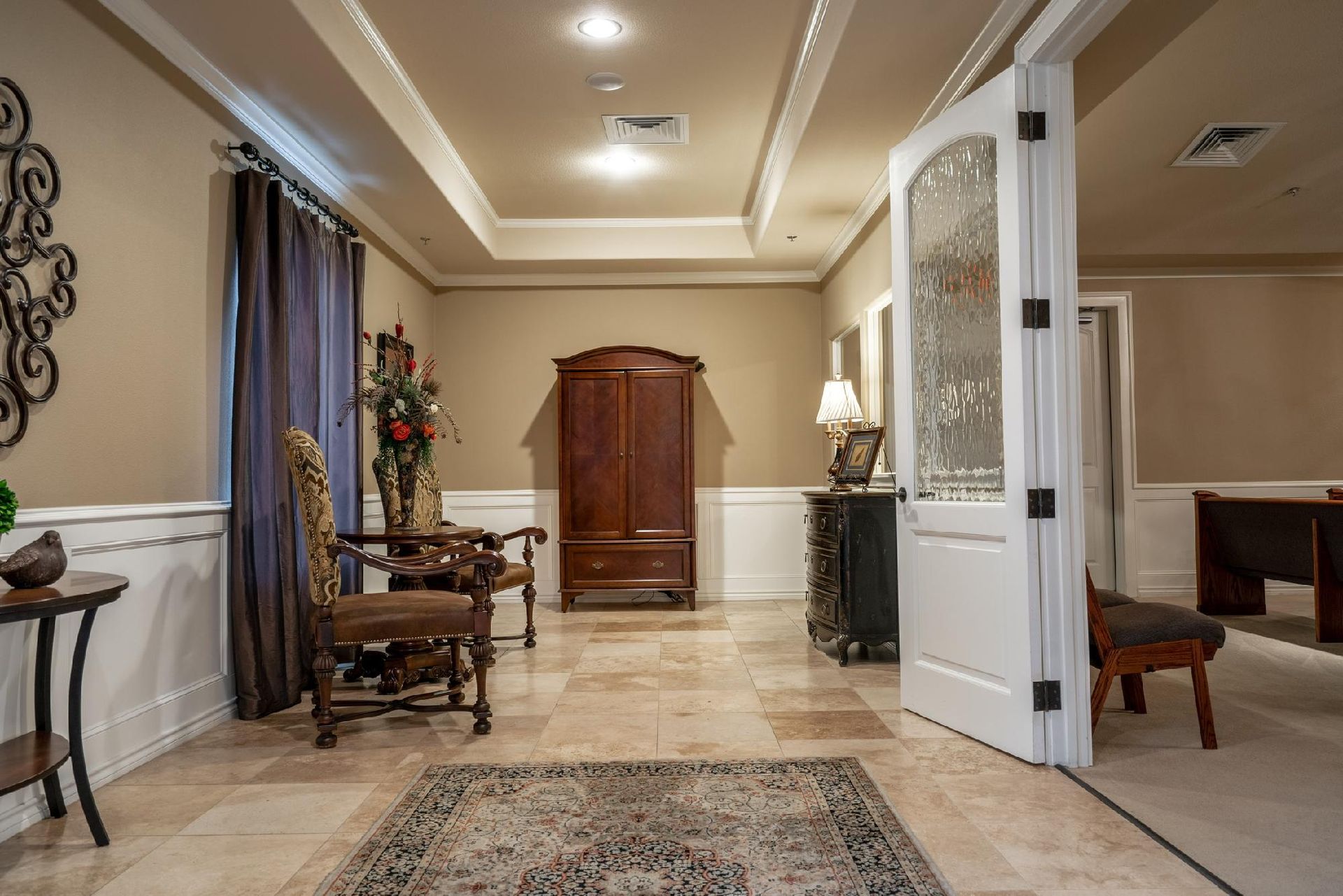 Elegant room with a dark wood armoire, ornate chair, open glass-paned door, and beige walls.