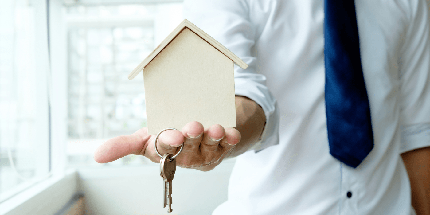 Hand holding a small house key, symbolizing home buying or property ownership