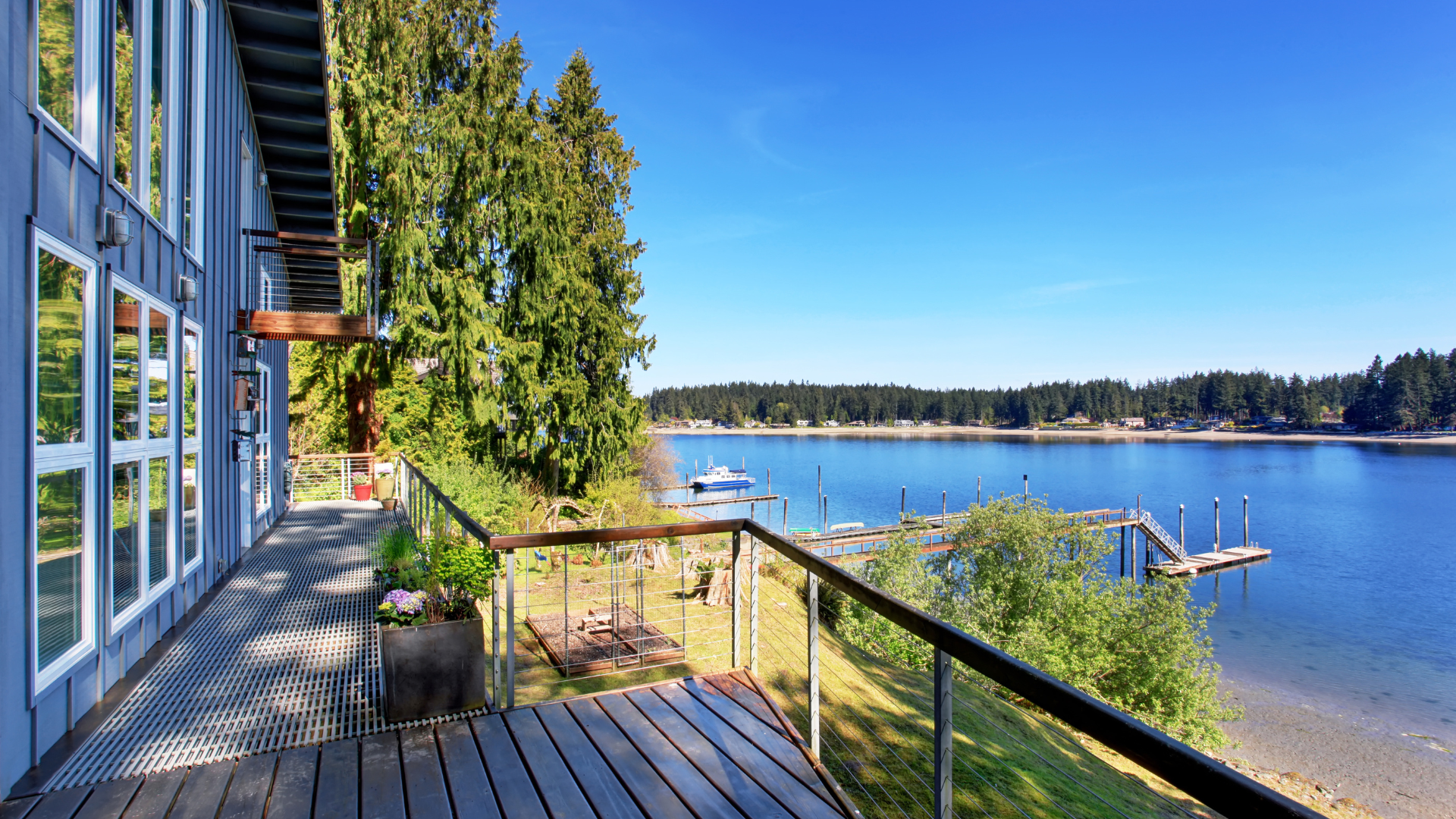 Wooden deck beside a blue waterfront house overlooking a calm bay under a clear sky