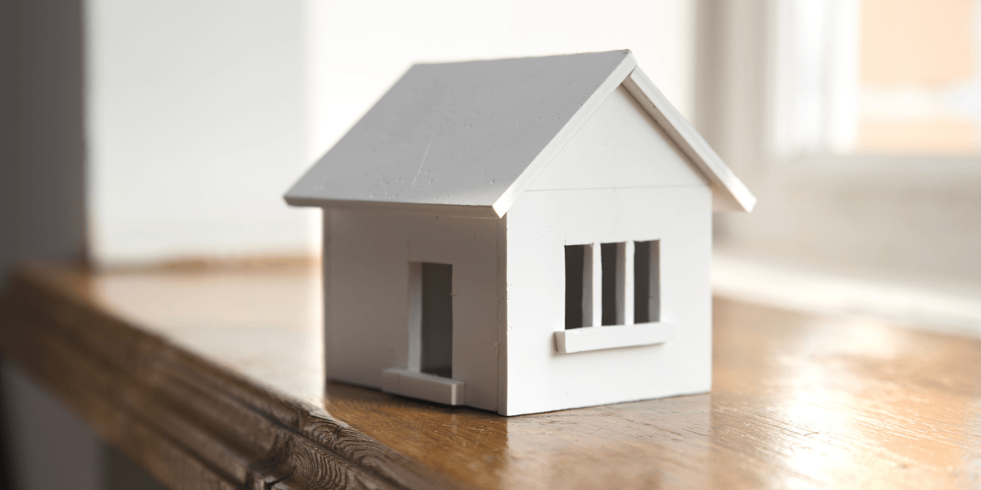 Small white model house on a wooden surface with a gray roof and soft background lighting