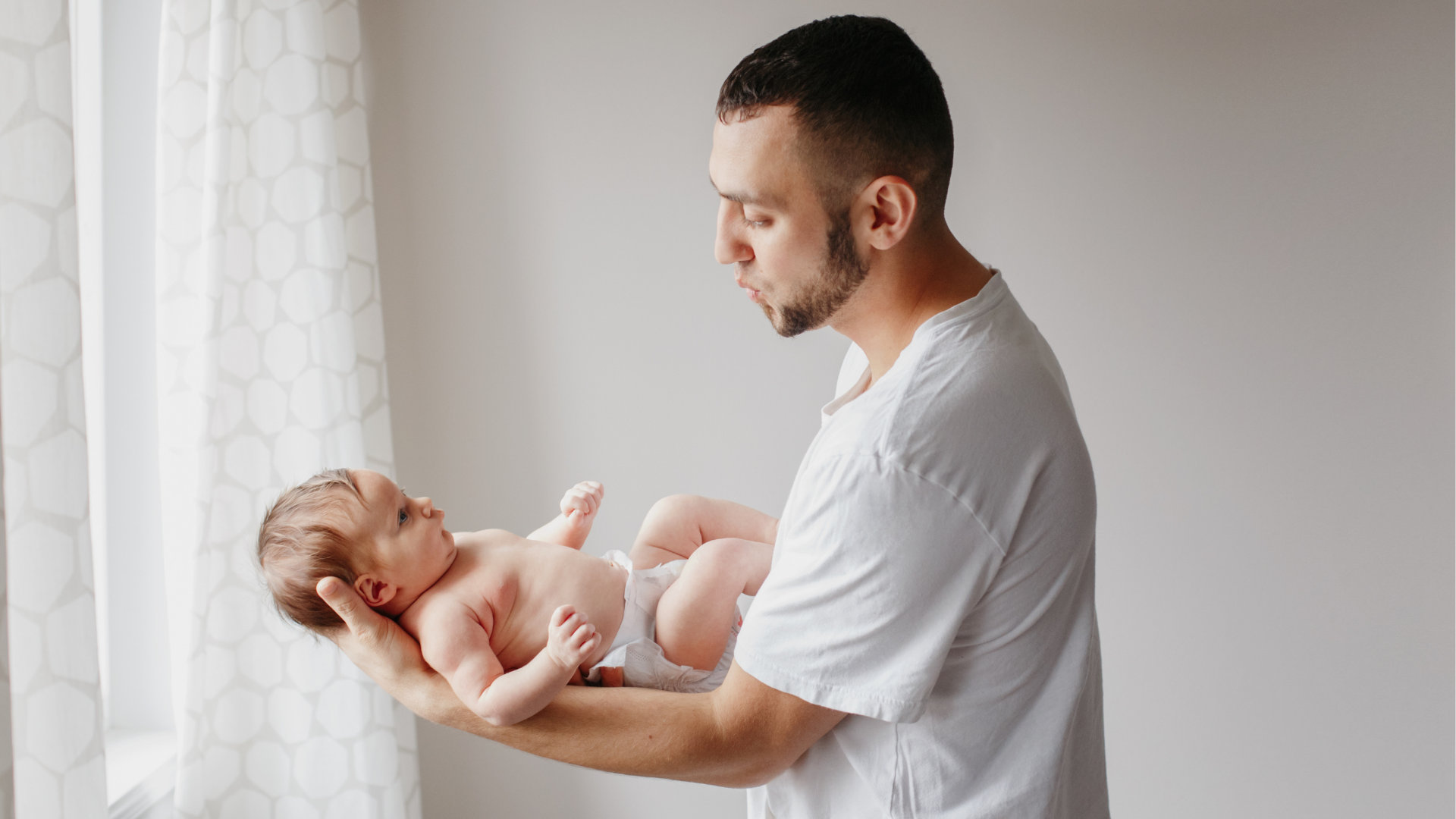 Man holding a baby near a bright window, looking down tenderly
