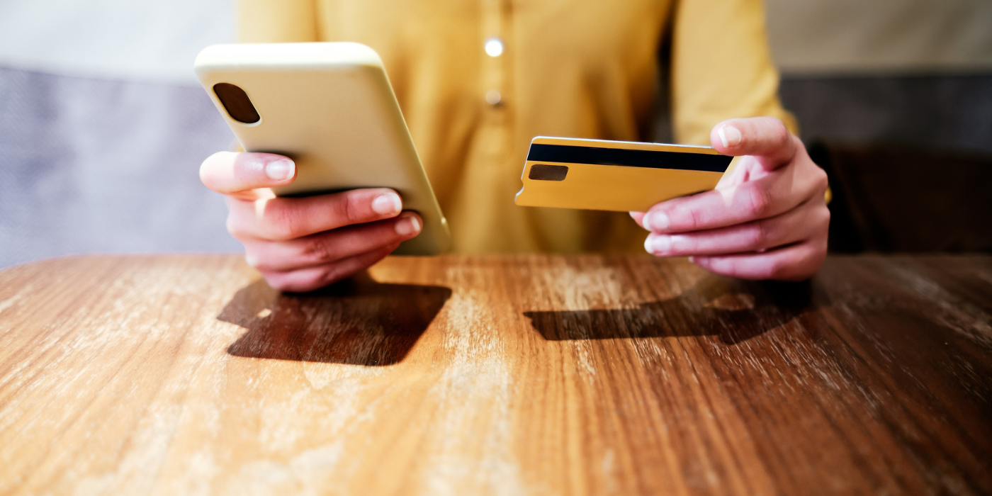 Hands holding a smartphone and a credit card over a wooden table with payment slots