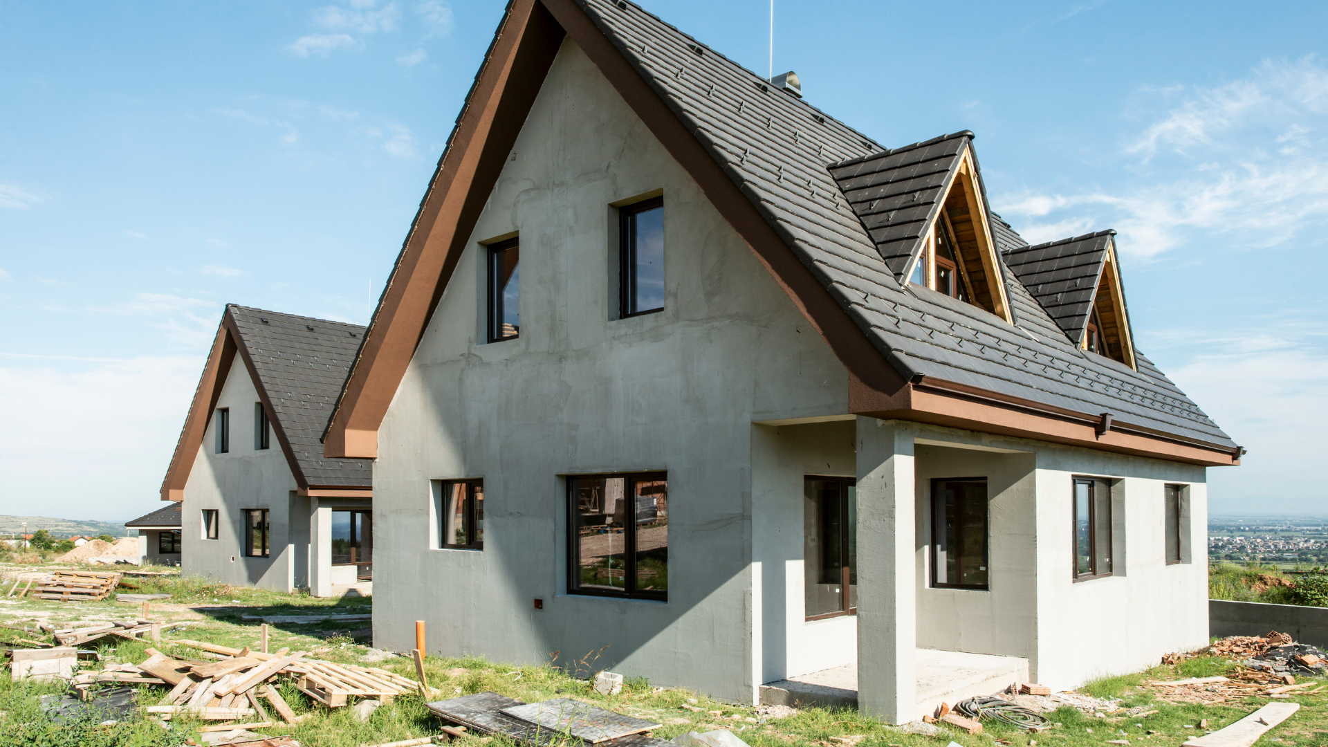 Two unfinished white houses with steep brown roofs at a construction site under a clear sky