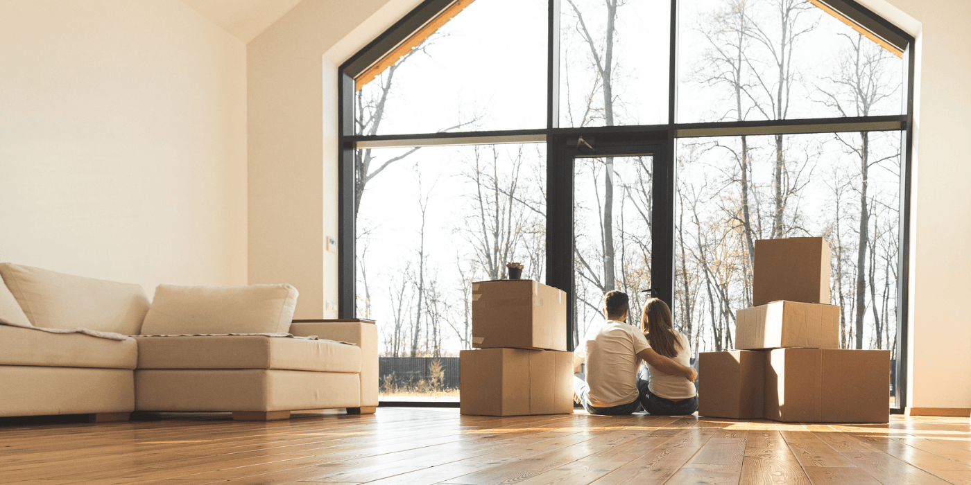 Bright living room with large windows, two children sitting on the floor, and moving boxes beside a sofa.