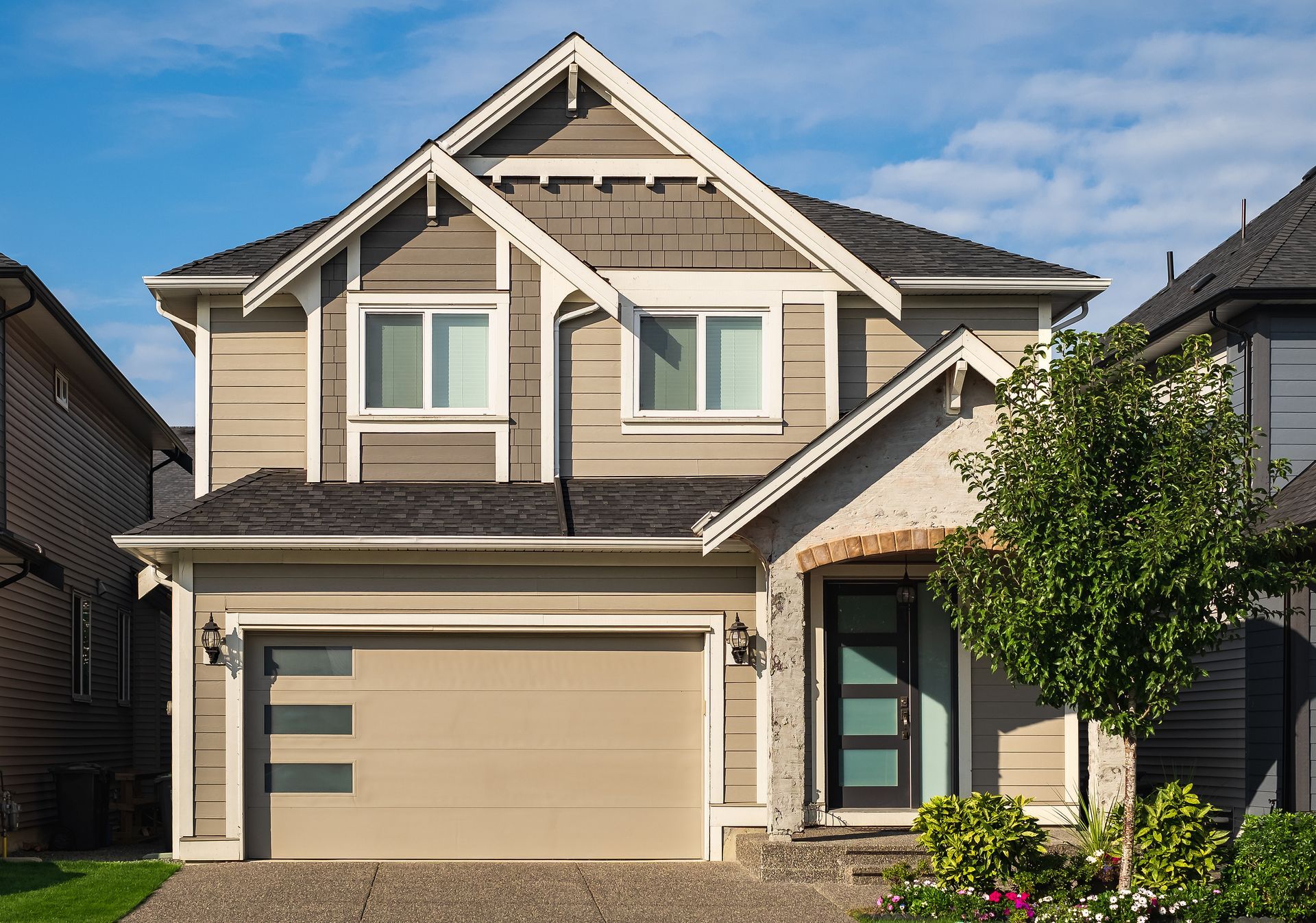 Modern two-story suburban house with tan garage door, gray siding, and a small front tree