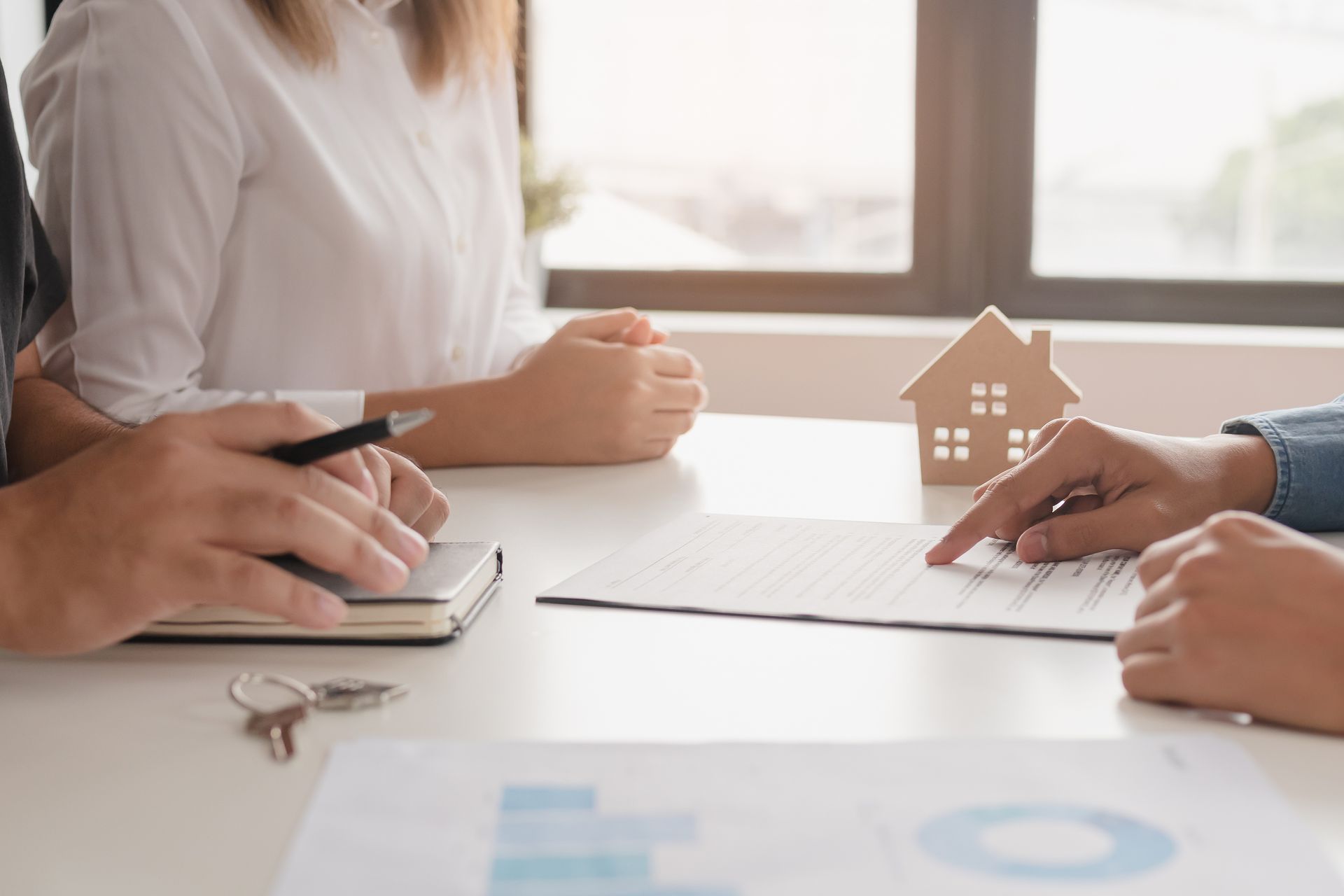 Three people reviewing house plans and a model home at a bright office table