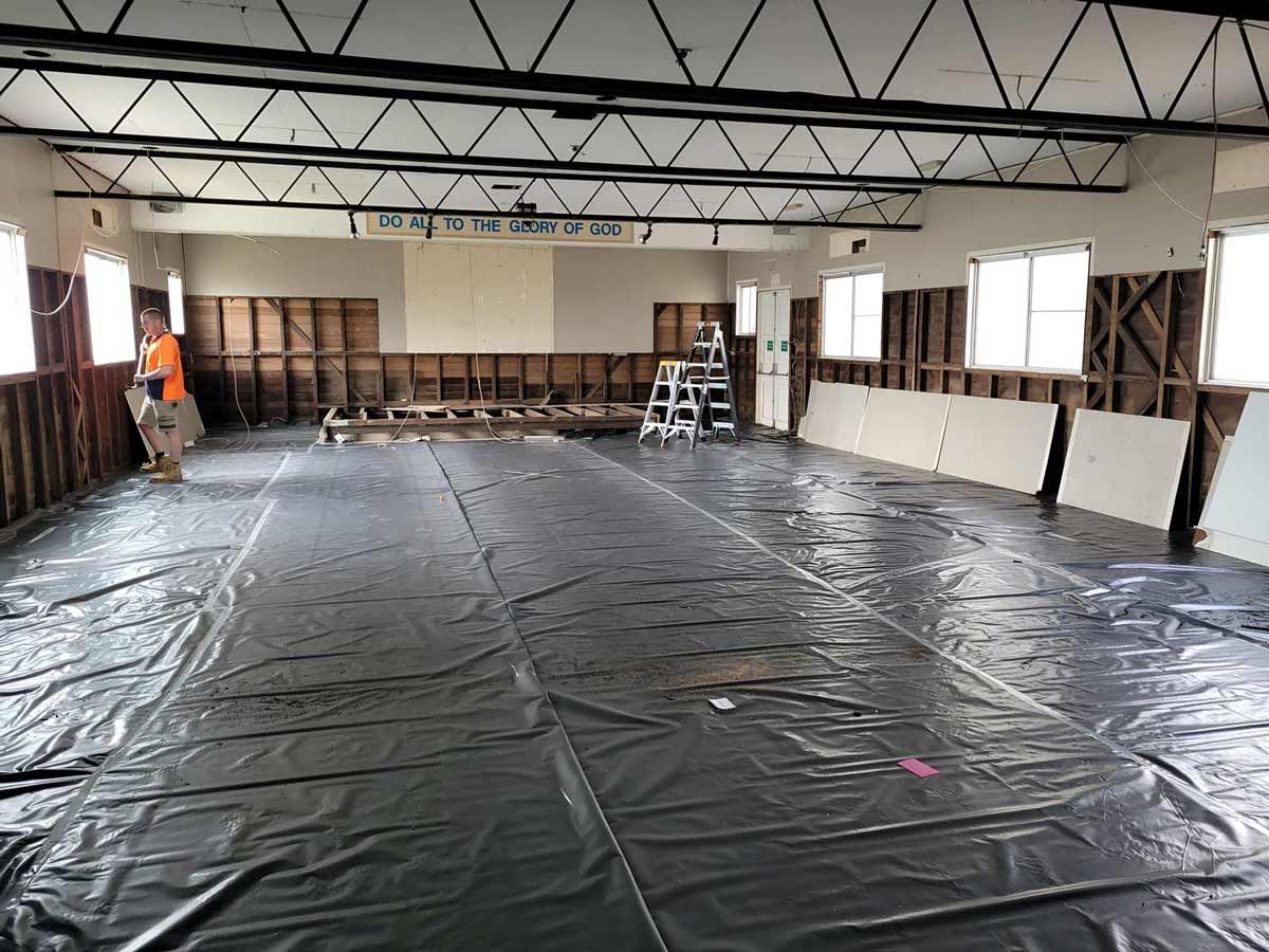 A Man Is Standing In A Large Room With A Plastic Tarp On The Floor — Accredited Asbestos Removers in Lismore, NSW