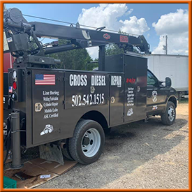 A black truck with a crane on the back is parked in a gravel lot.