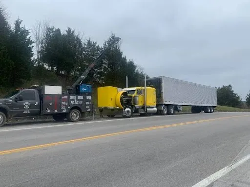 A tow truck is towing a semi truck on the side of the road.