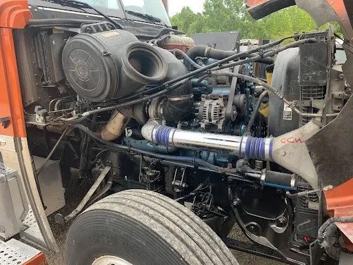Open engine compartment of an orange semi-truck. Various engine components, including a large air filter and blue hose, are visible.