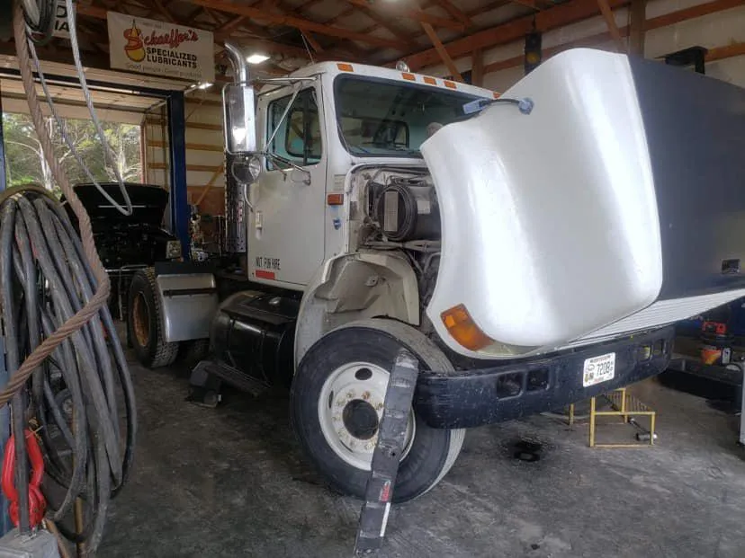 A white truck is sitting in a garage with the hood up.