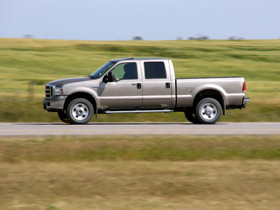 A silver pickup truck is driving down a road.