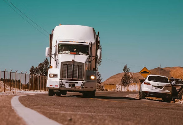Semi-truck driving down a rural road under a teal sky, seen from a low angle