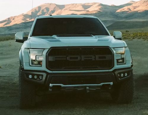 White Ford pickup truck with a black grille parked on a dirt road with mountains in the background