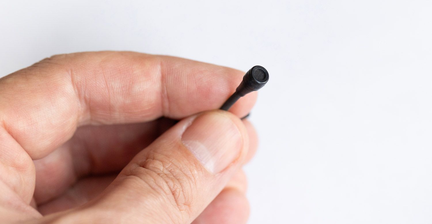 Close-up of a tiny listening device held between fingers, illustrating the compact size and discreet nature of modern surveillance technology