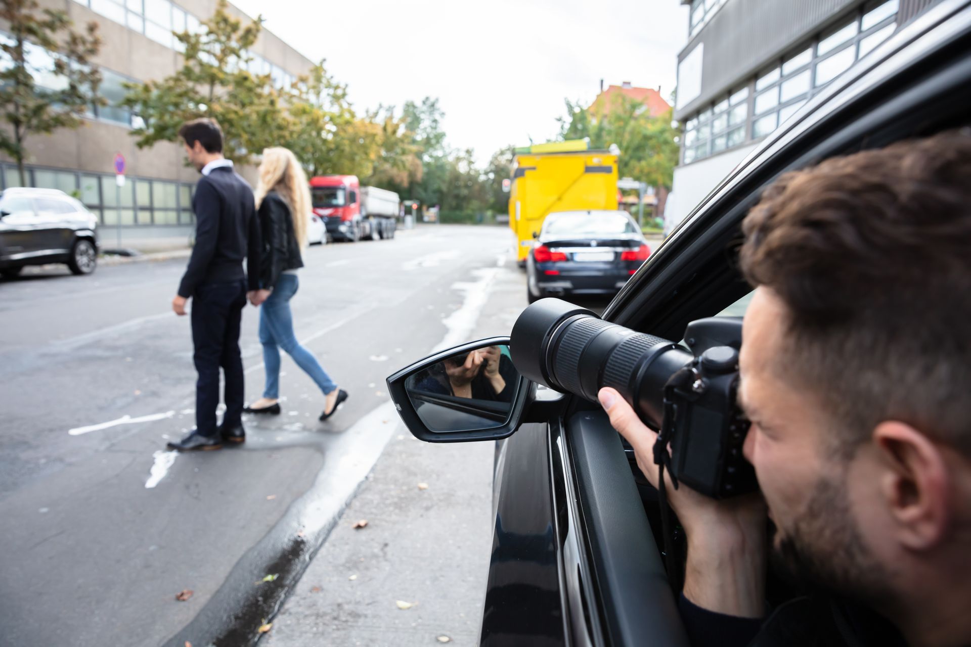Person with camera in car takes photos of couple crossing street.