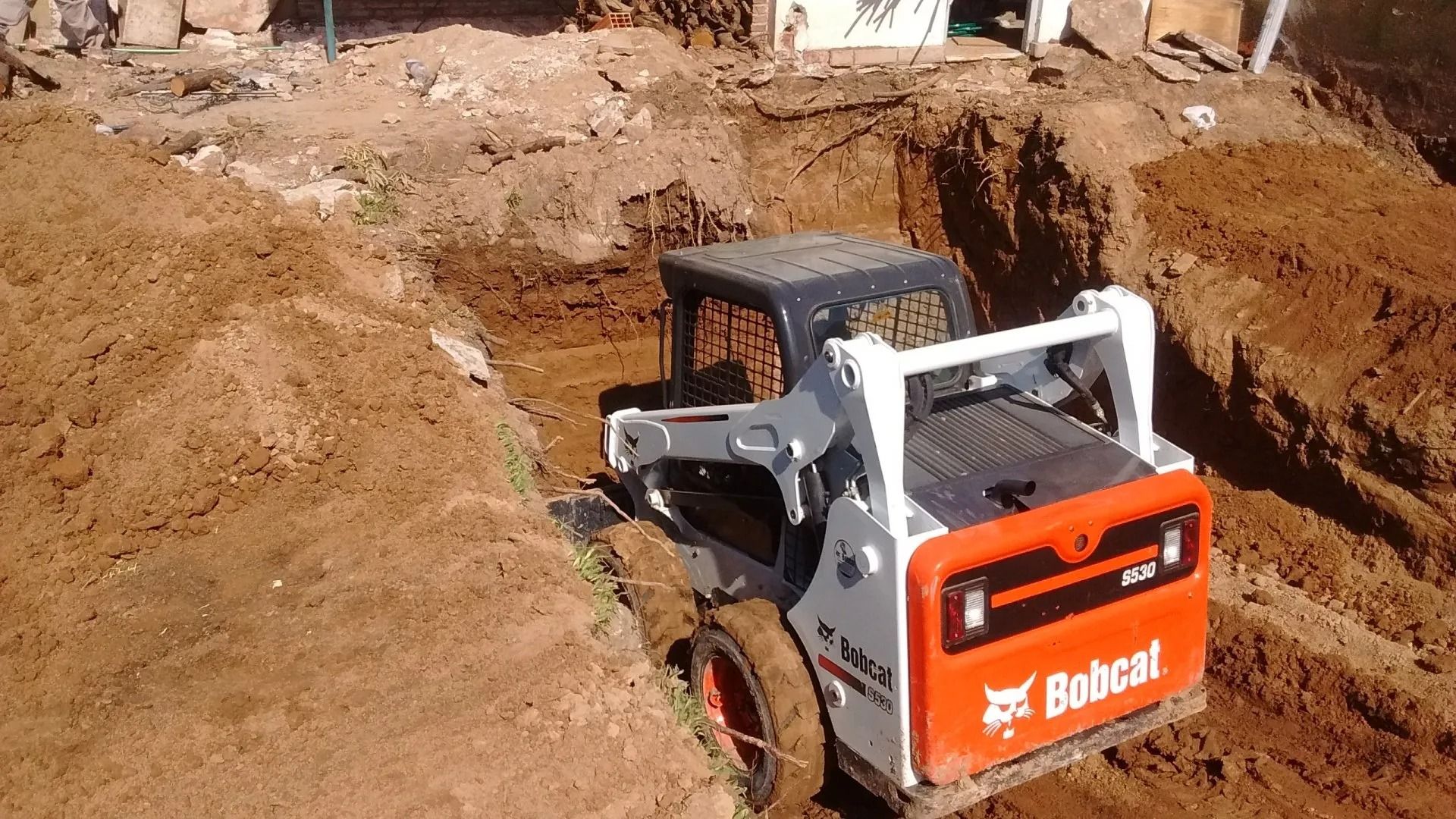 Minicargadora Bobcat cavando una zanja en una obra de construcción de tierra.