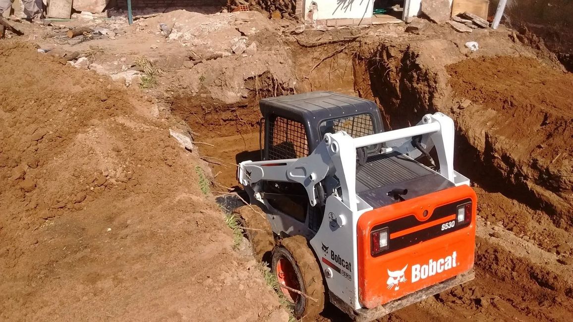 Minicargadora Bobcat cavando una zanja en una obra de construcción de tierra.