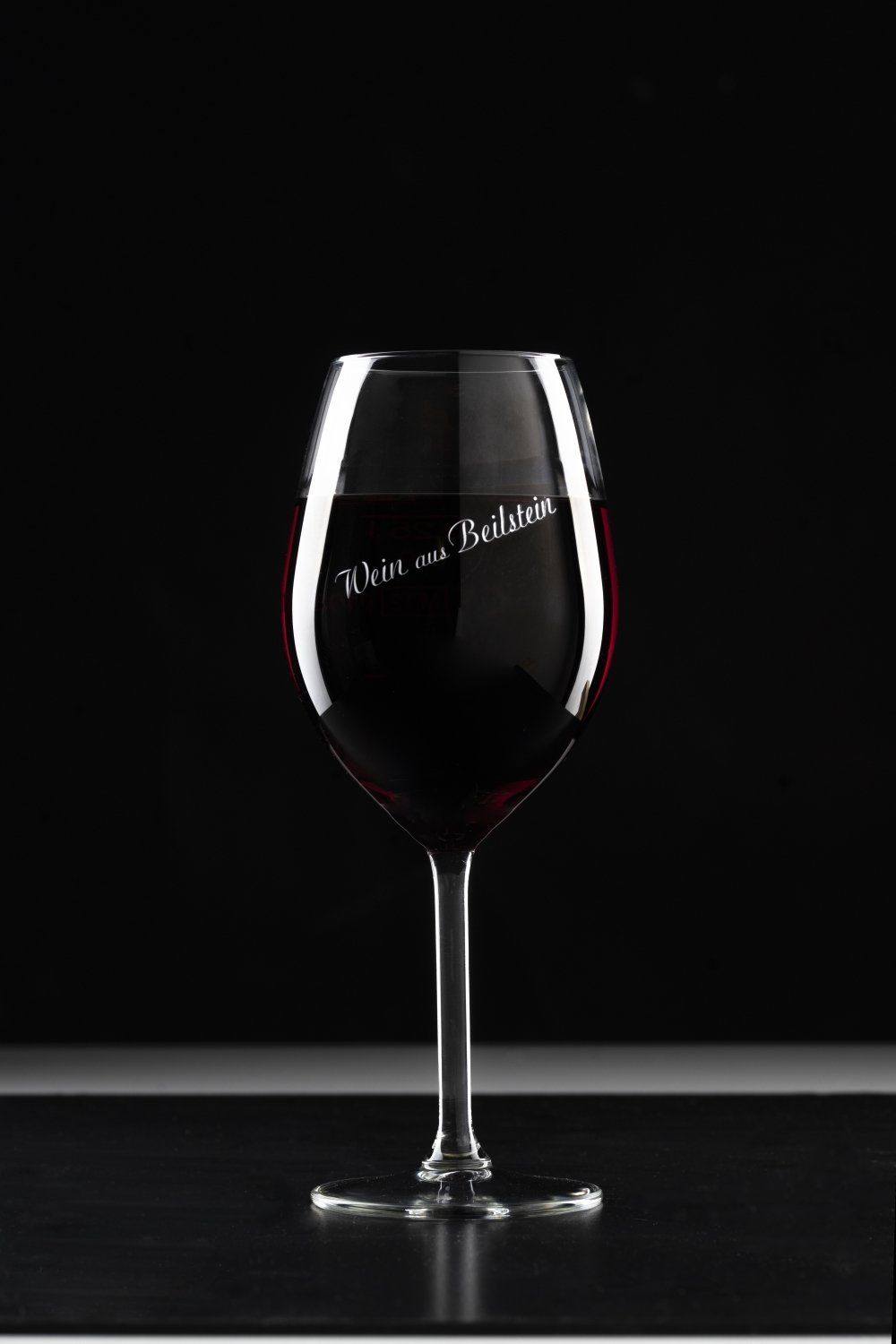 Ein Glas Rotwein steht auf einem Tisch vor schwarzem Hintergrund.