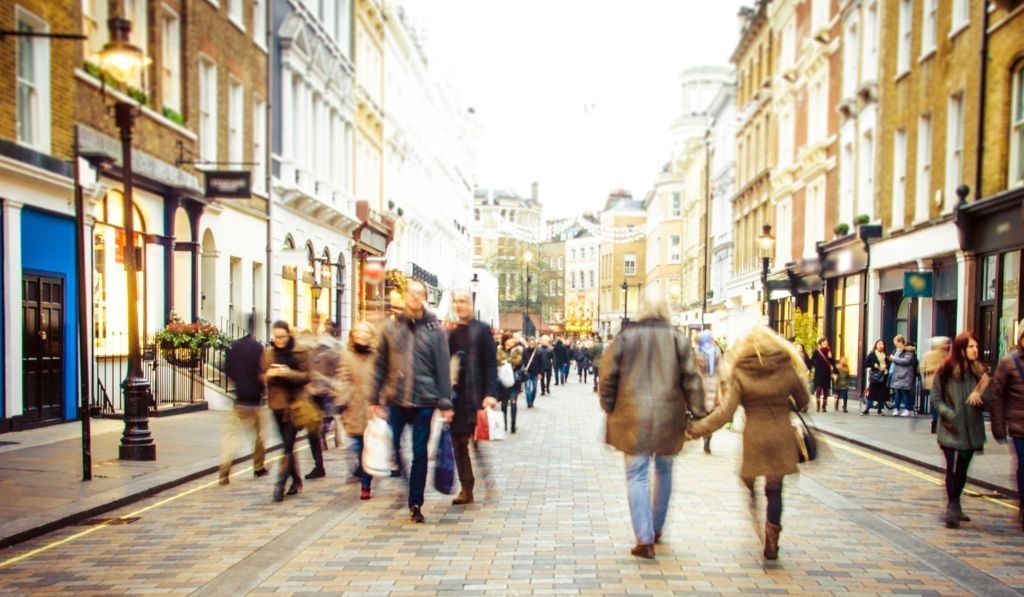 Des gens marchant dans une rue animée bordée de magasins et de bâtiments, sous la lumière chaude du soleil, des mouvements flous.