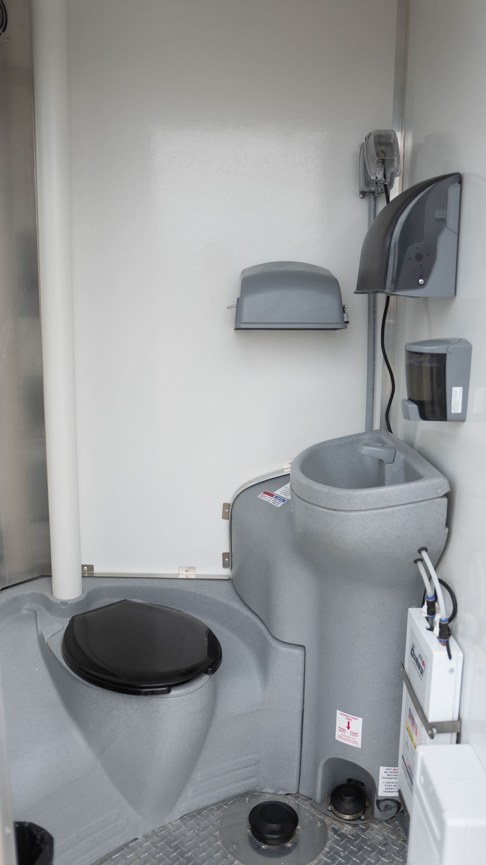 Interior view of a gray portable toilet with a toilet seat, sink, and soap dispenser.