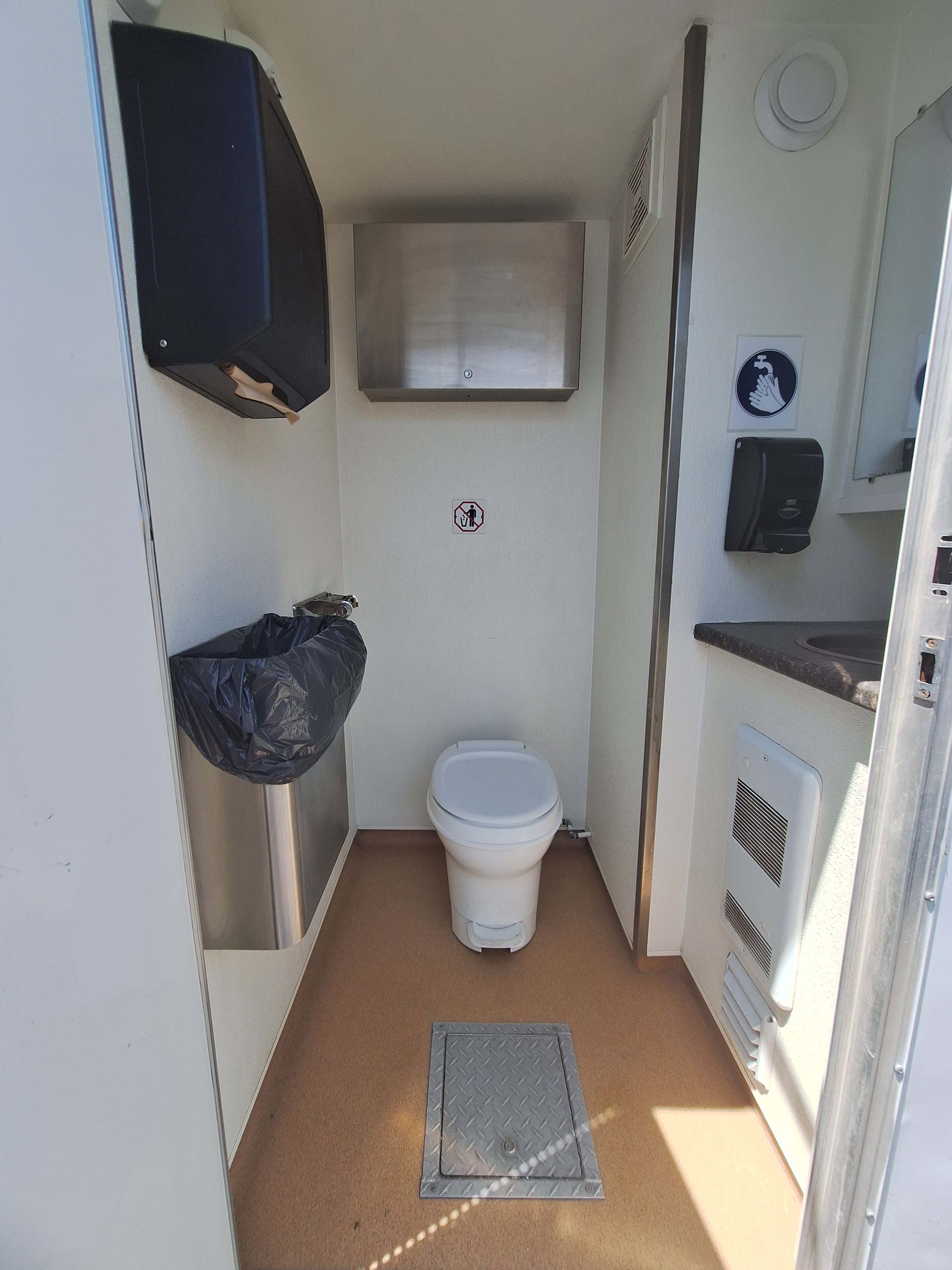 Interior of a portable restroom with a toilet, sink, and hand sanitizer dispenser.
