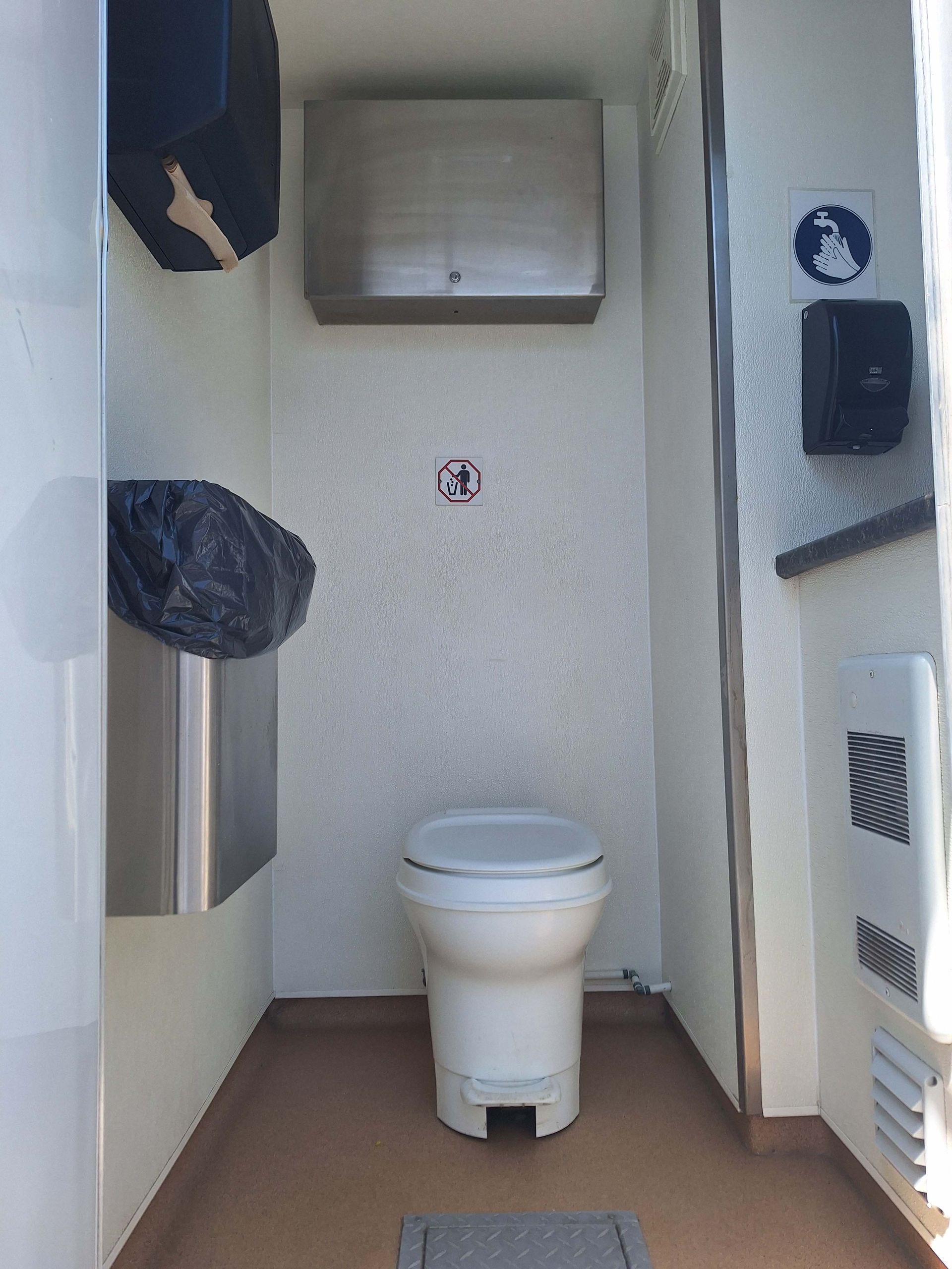 Toilettes portatives argentées dans un terrain en gravier par une journée ensoleillée; « BC29 » sur le côté.