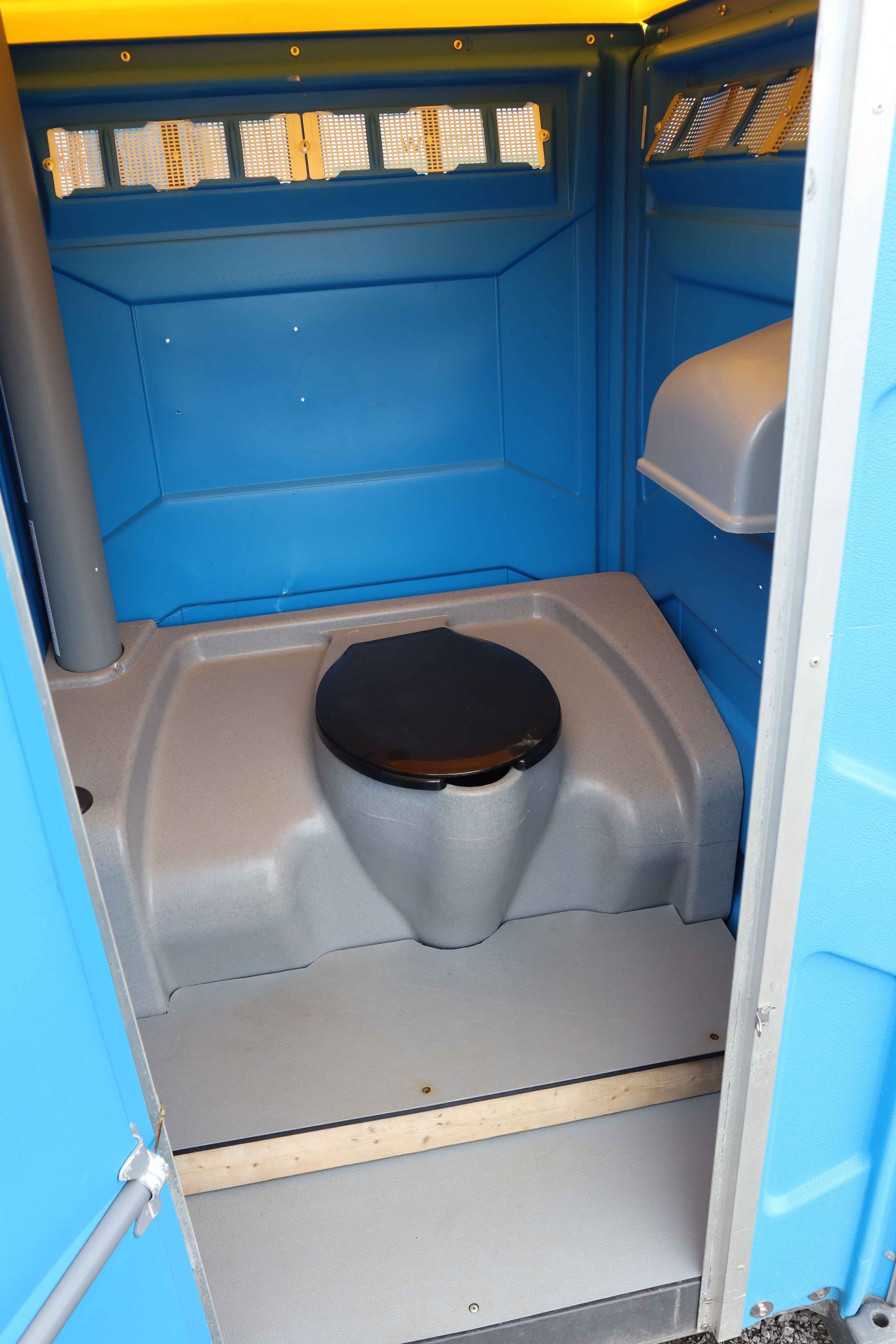 Toilettes portables bleues et jaunes sur une surface rouge dans un parc, avec des équipements de jeux en arrière-plan.