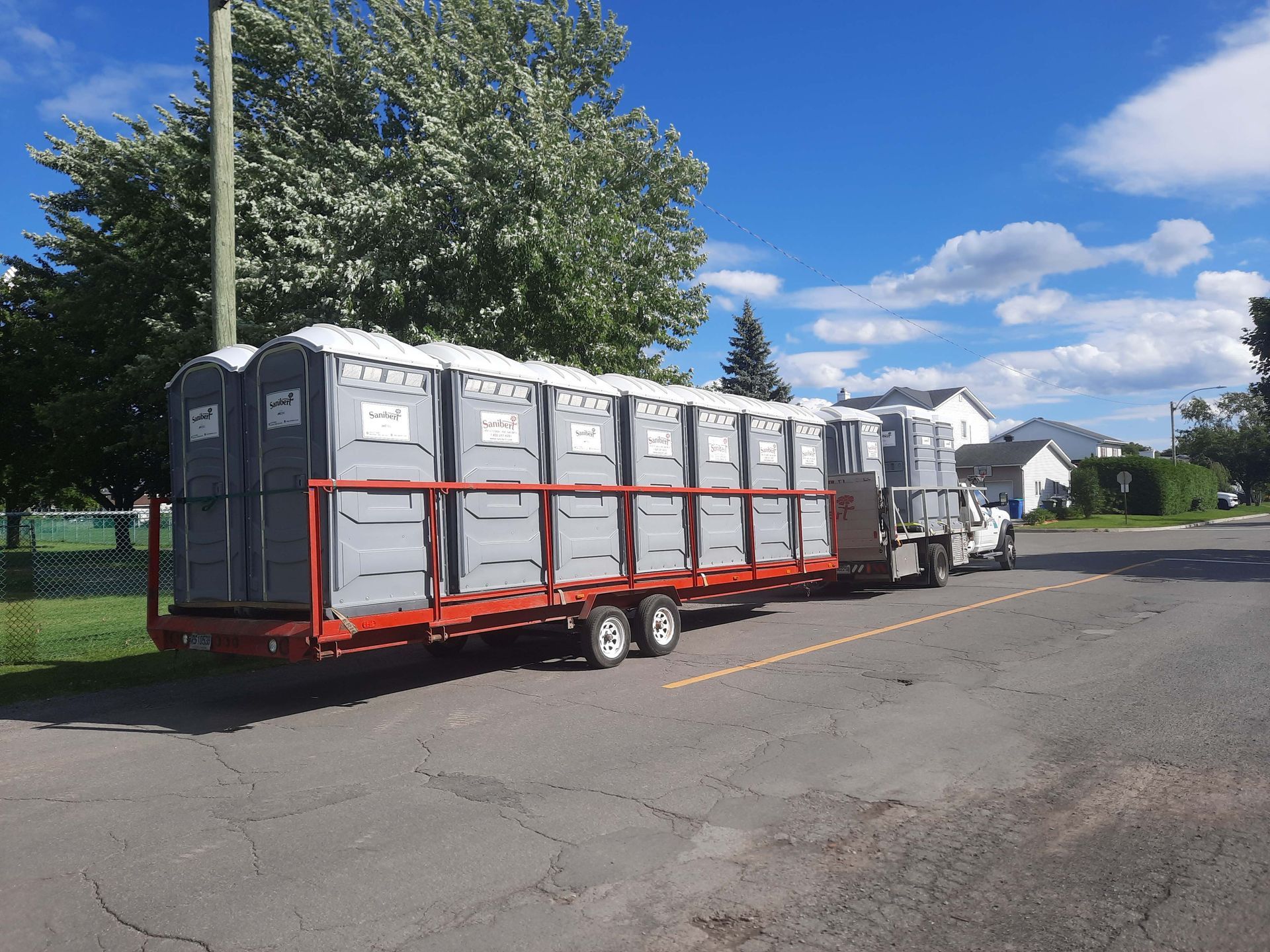 Camion transportant une remorque chargée de nombreuses toilettes portables par une journée ensoleillée.
