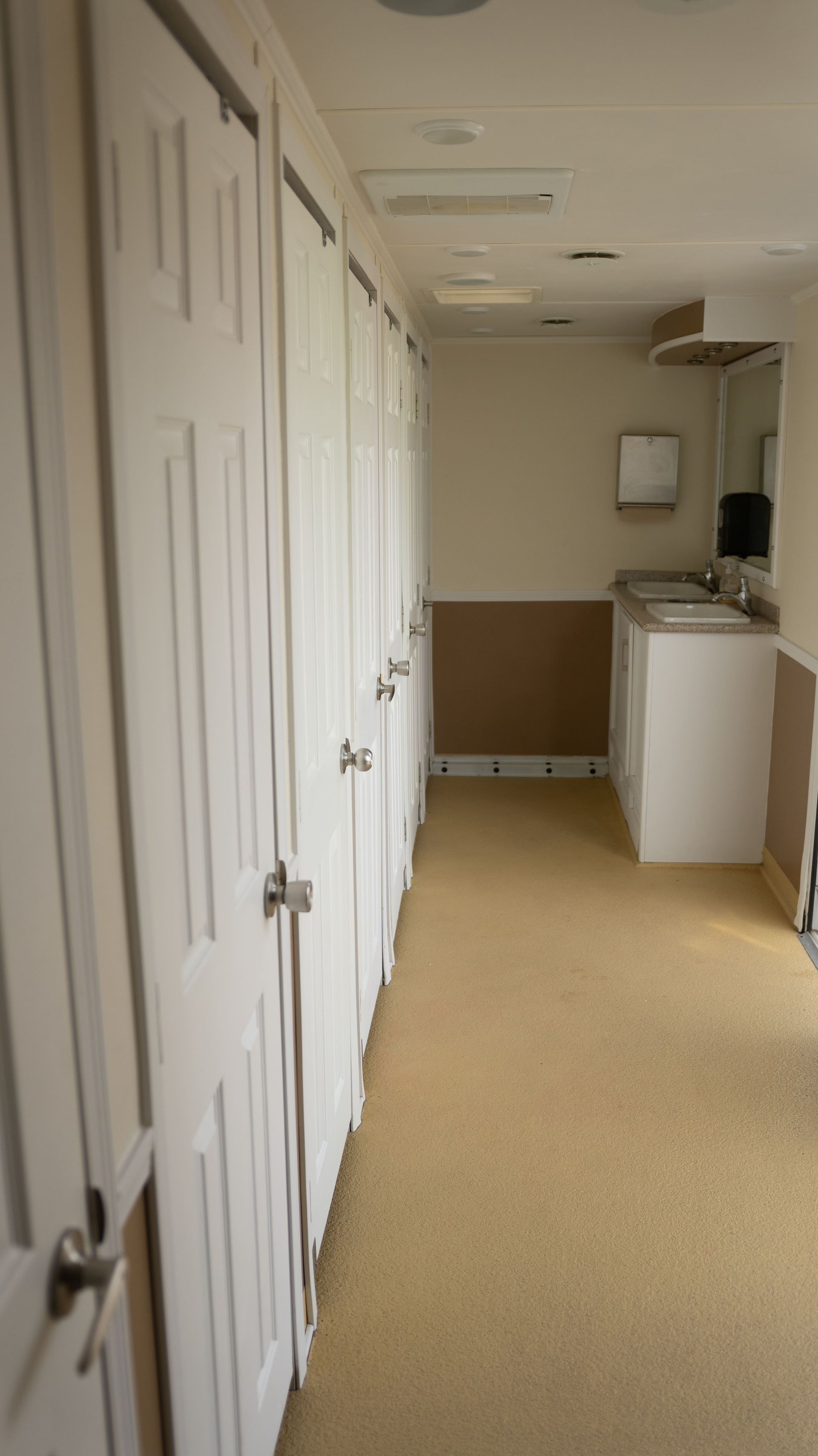 Remorque de toilettes portables blanches avec plusieurs stalles, stationnée à l'extérieur.