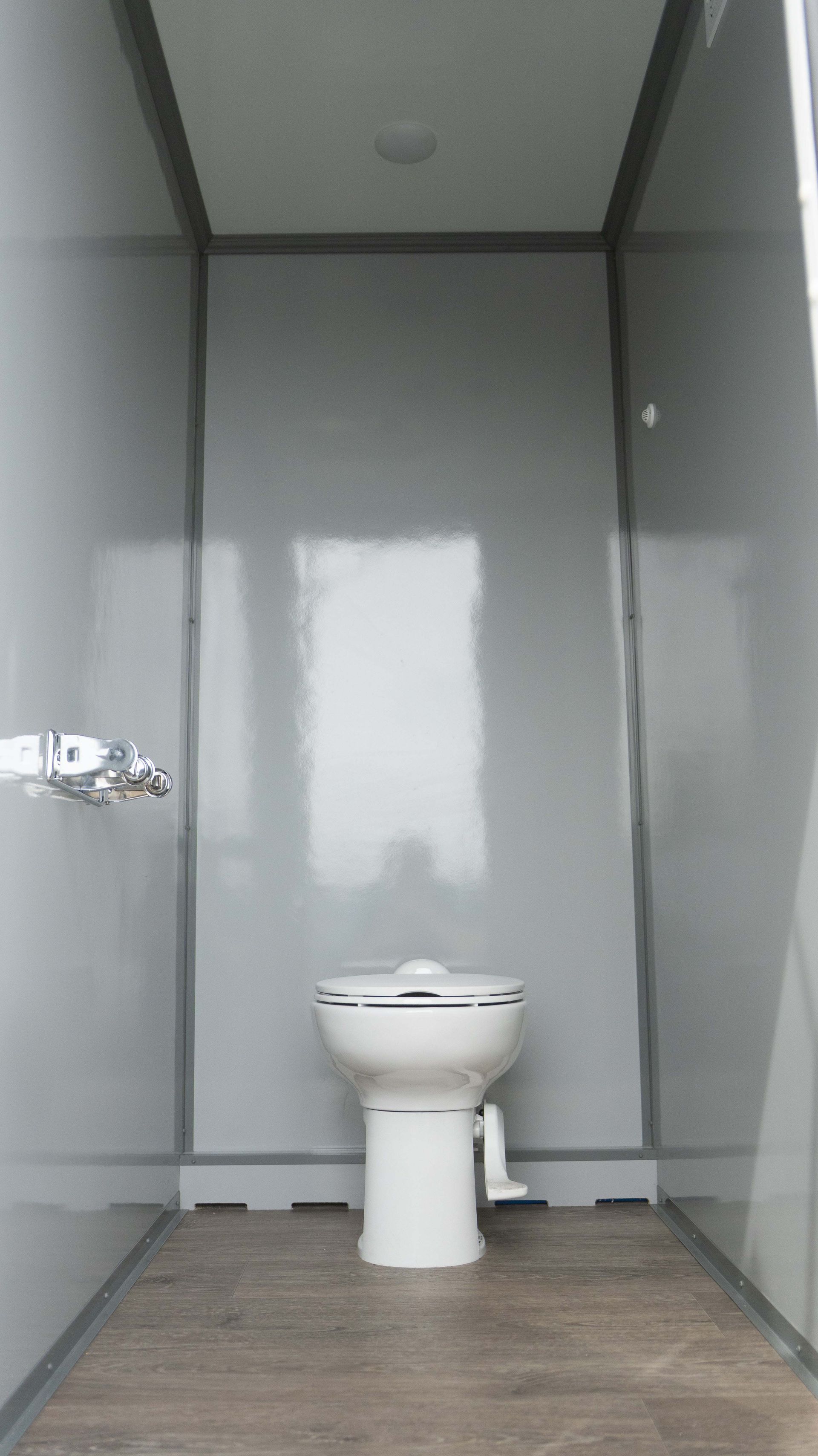Remorque de toilettes portables blanches avec deux portes, marches et un pneu, à l'extérieur.