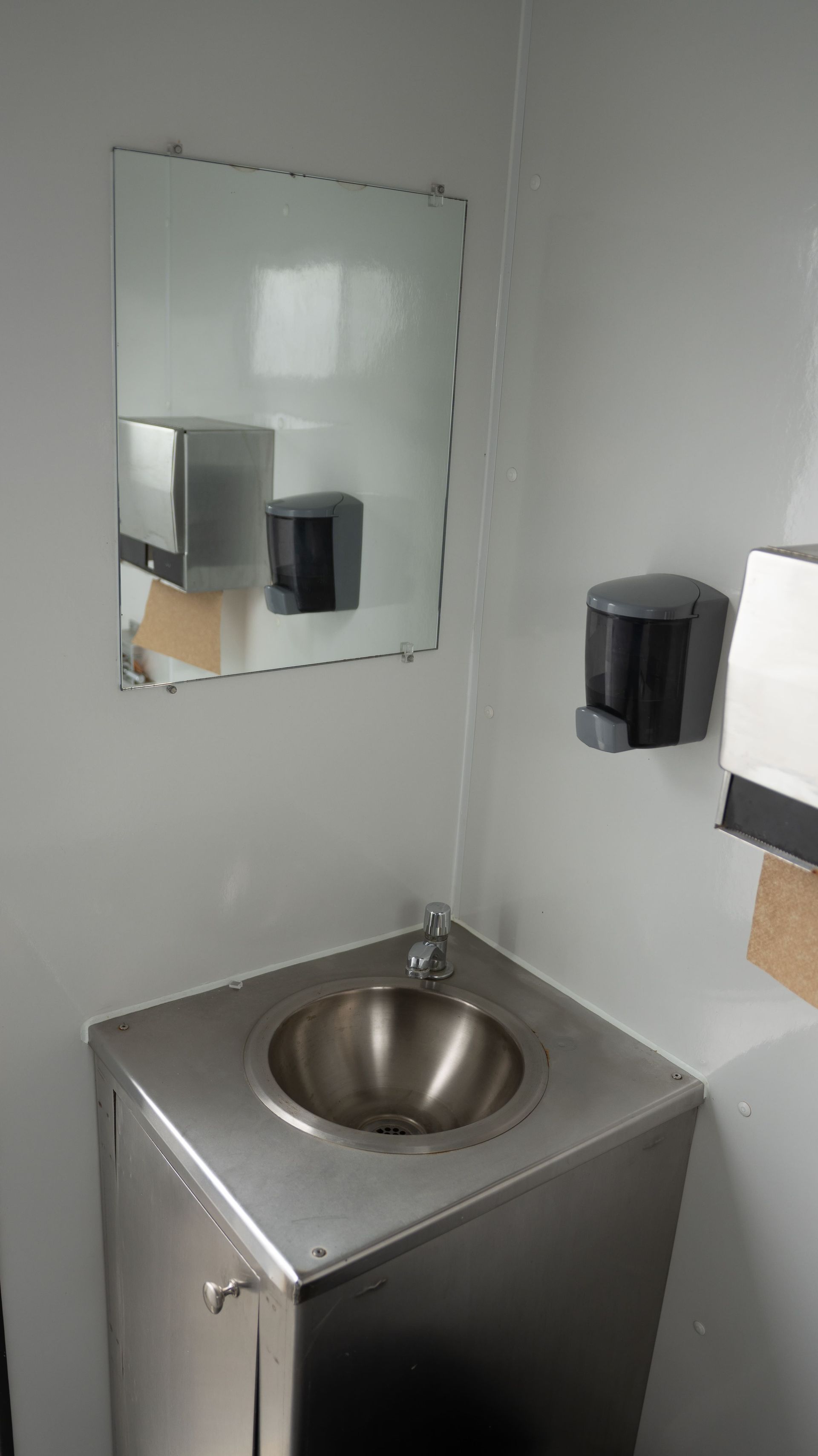 Remorque de toilettes portables blanches sur gravier contre un ciel nuageux.