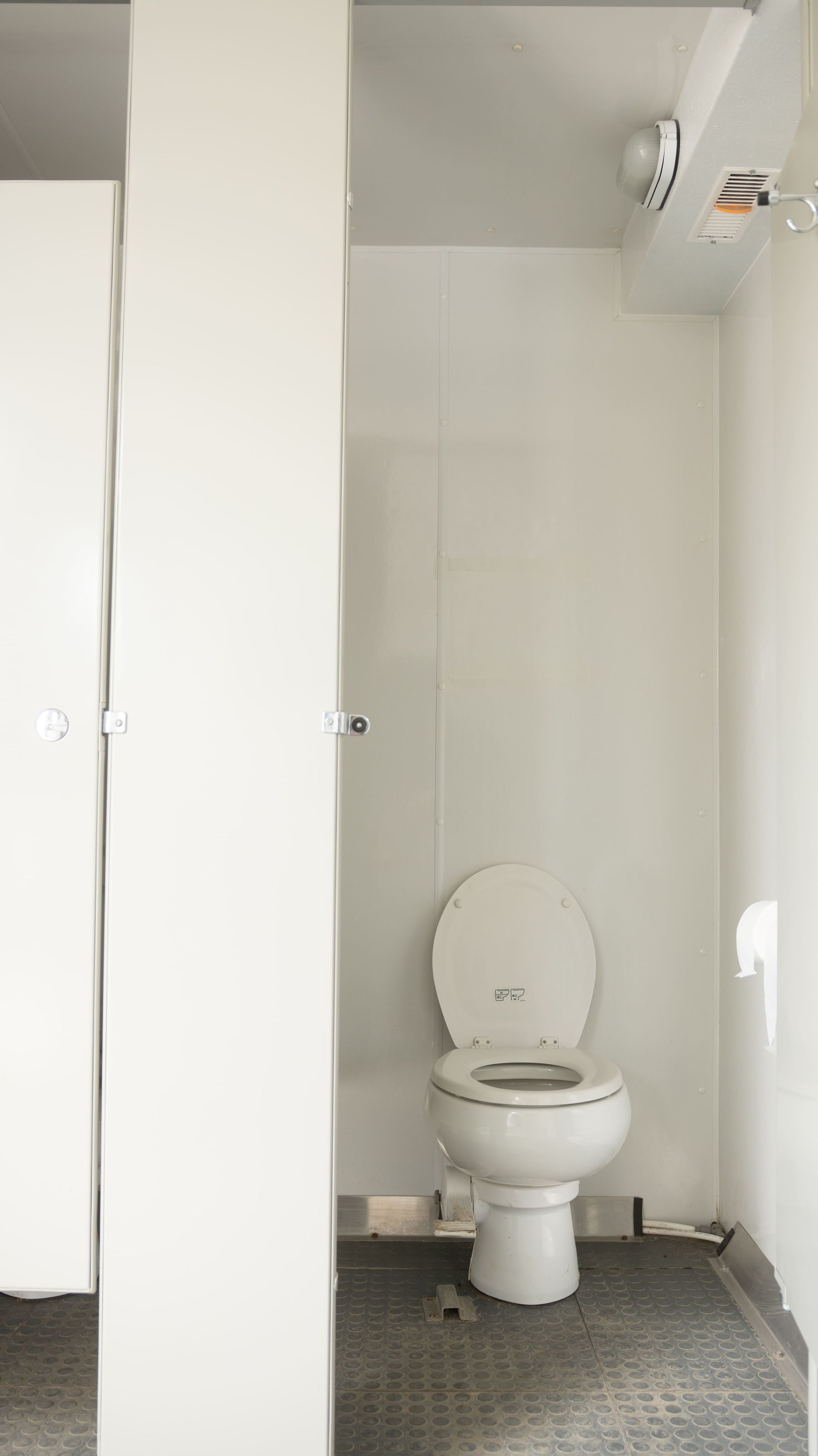 Remorque de toilettes portables blanches sur un terrain en gravier avec lettrage rouge.