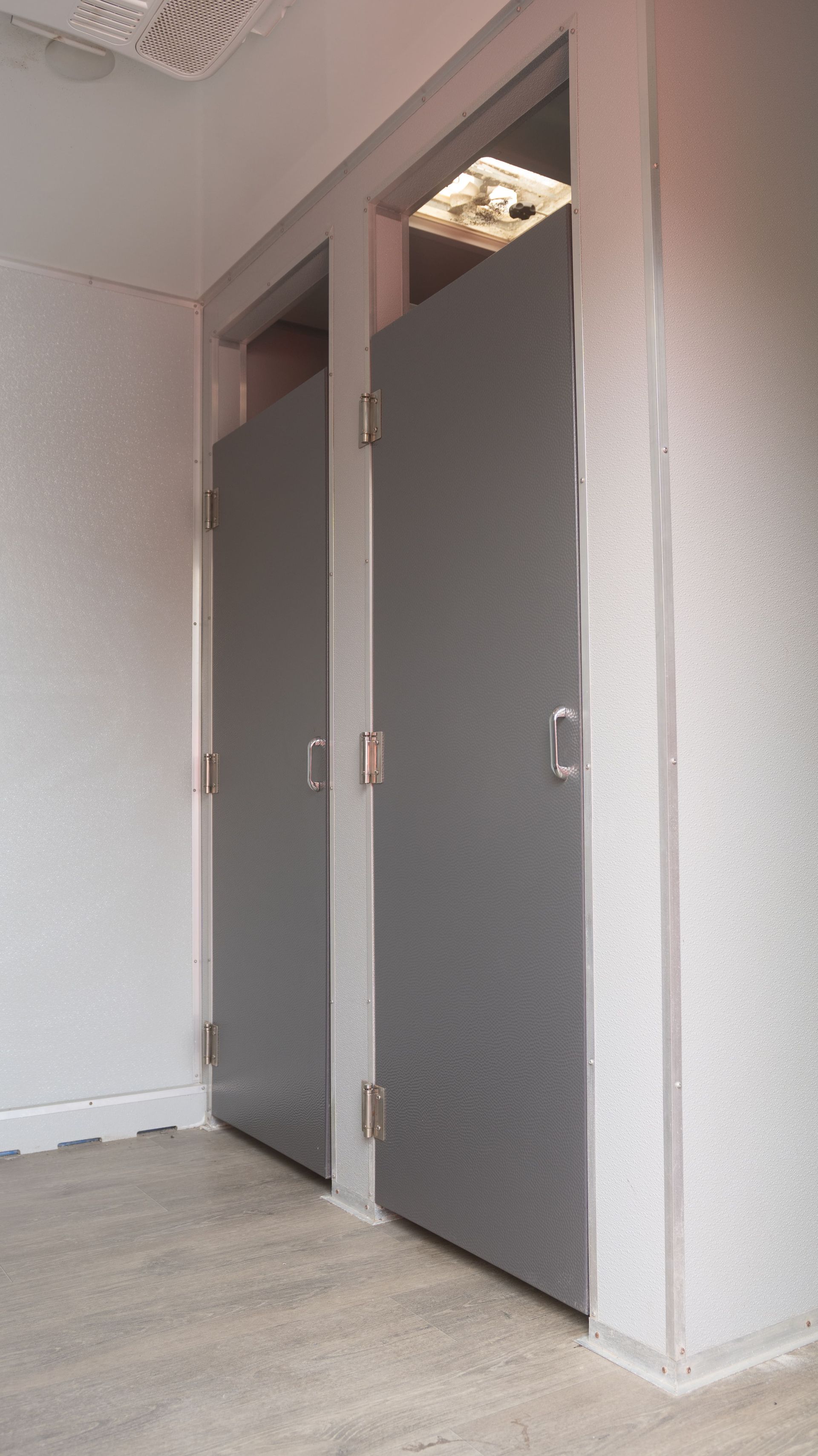 Remorque de toilettes portables blanches avec logo rouge sur un terrain en gravier sous un ciel nuageux.
