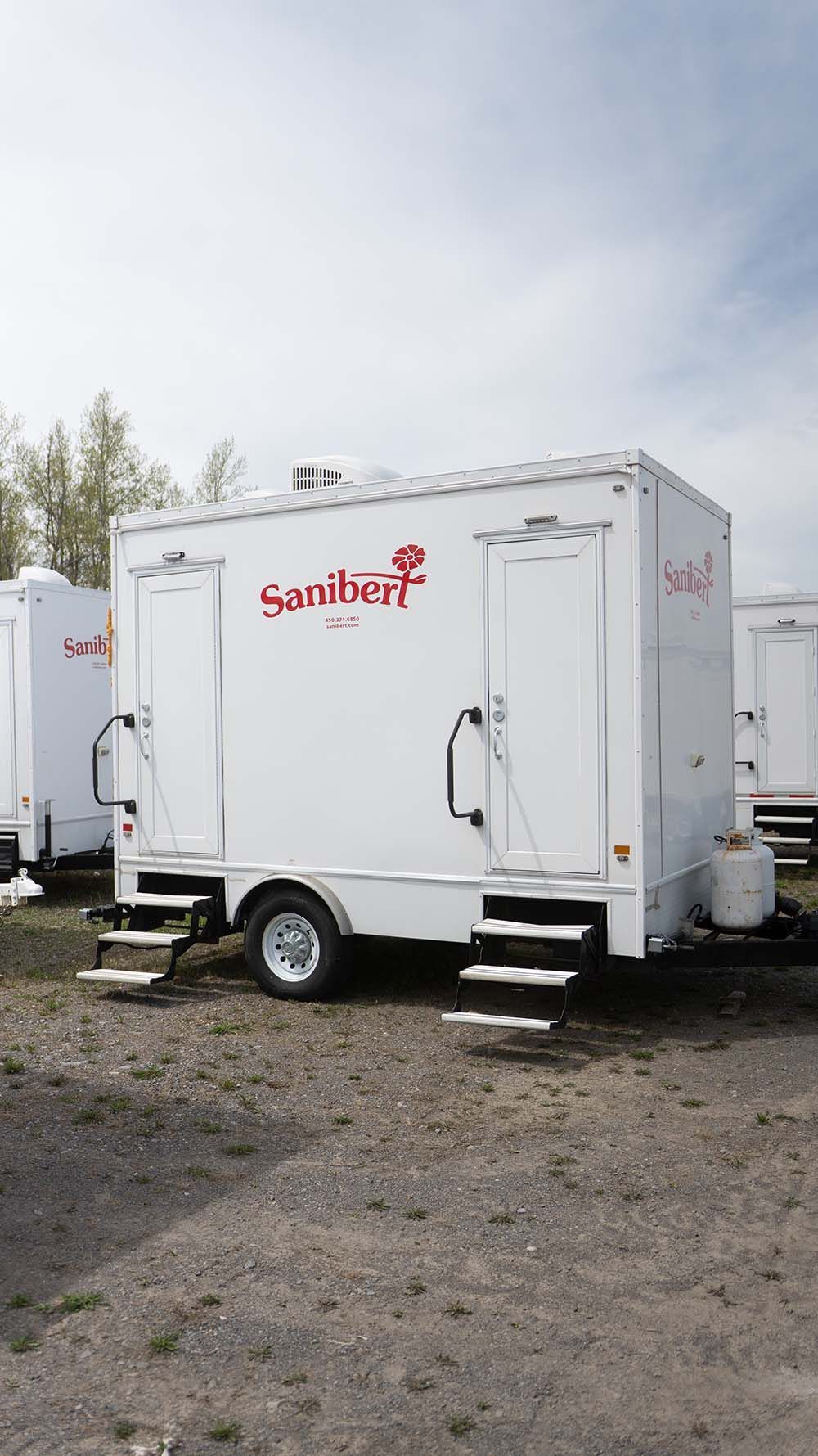 Remorque de toilettes portables blanches avec escaliers, marquée « Sambert » en rouge, garée à l'extérieur.