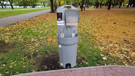 Station de lavage des mains portable dans un parc ; grise, avec savon, essuie-mains en papier et bouteilles d'eau.