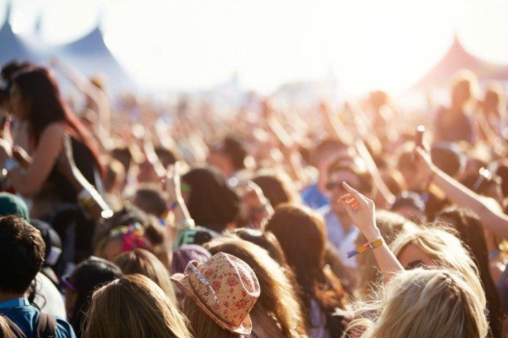 Foule lors d'un concert en plein air avec les mains levées, la lumière du soleil et des tentes en arrière-plan.