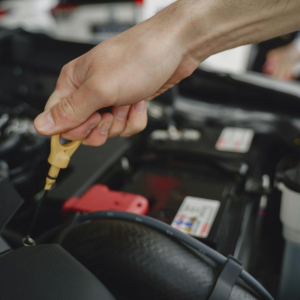 A hand holds an engine oil dipstick while checking fluid levels inside a car's open engine bay.