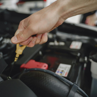 A hand holds an engine oil dipstick while checking fluid levels inside a car's open engine bay.