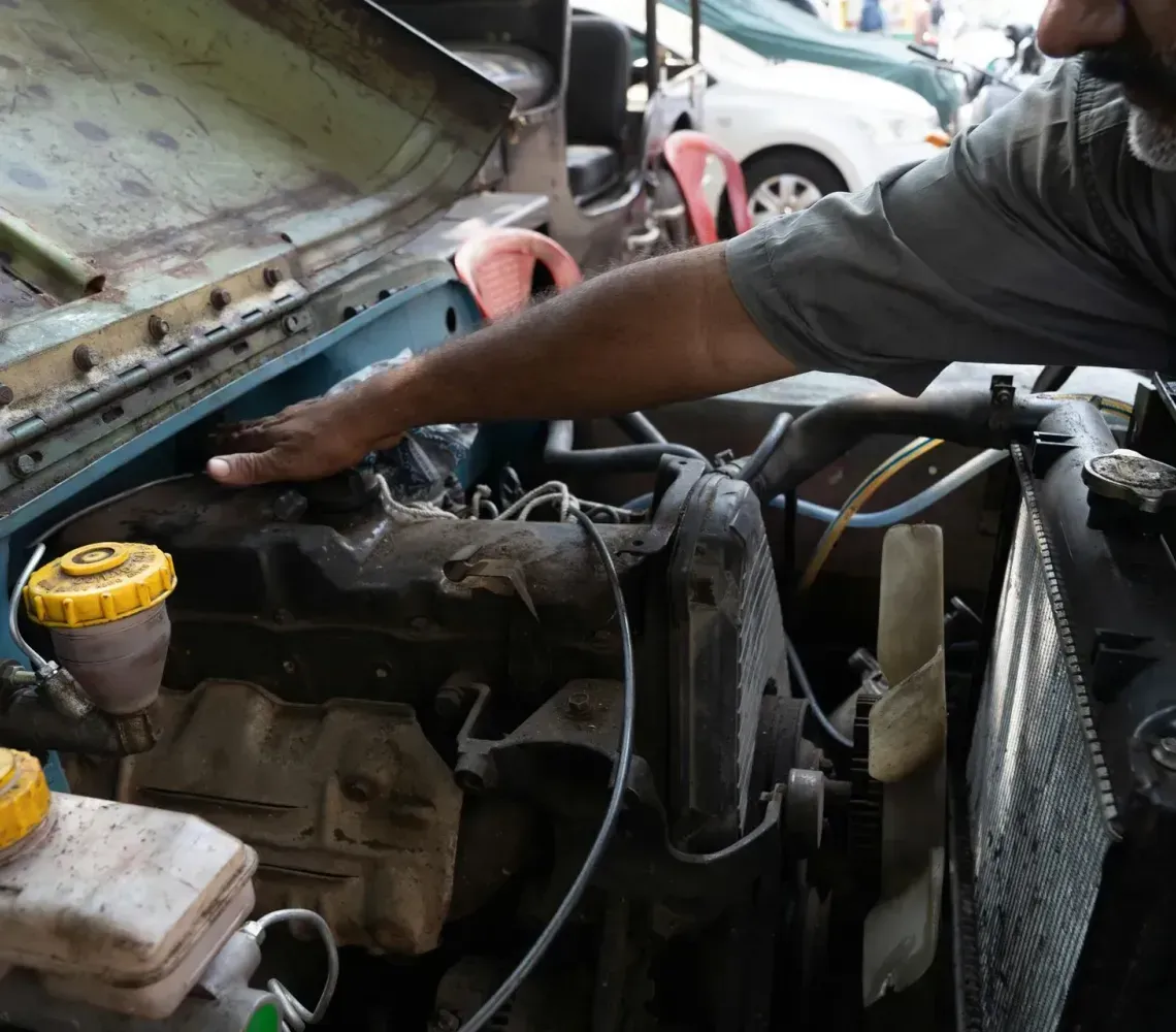 A mechanic works under the open hood of a vehicle, inspecting the engine components.