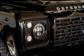 Close-up of the front black grille and headlight assembly of a Land Rover Defender vehicle.