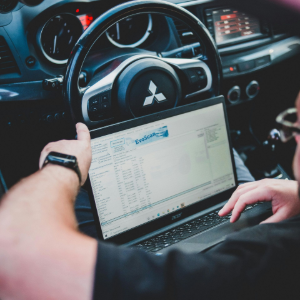 A person inside a Mitsubishi car uses a laptop to tune or diagnose the vehicle's engine management system.