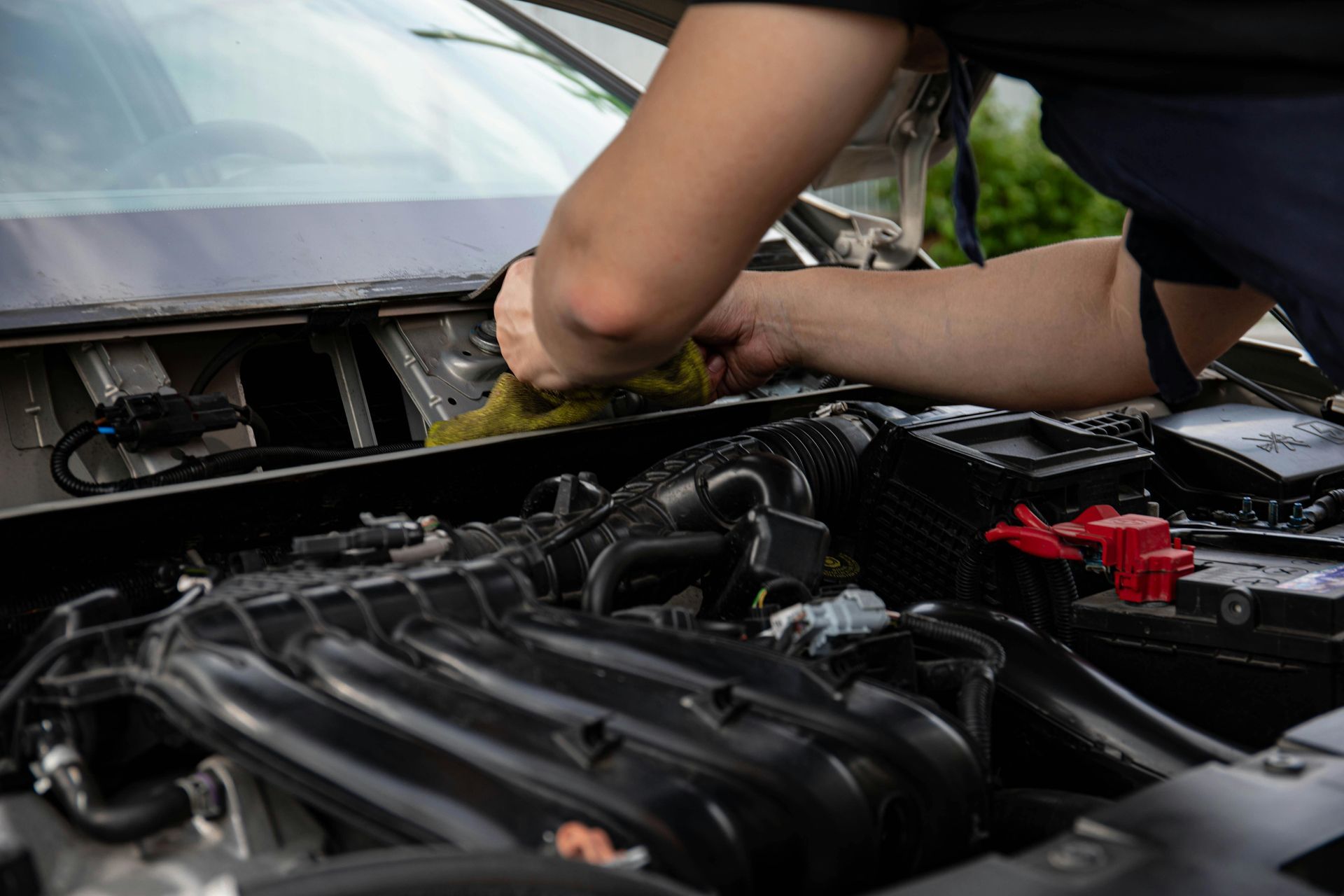 A mechanic wipes down the area beneath the windshield of a car with an open hood.