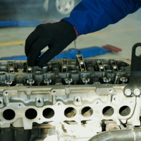 A gloved mechanic works on the exposed engine block of a vehicle in an auto repair shop.