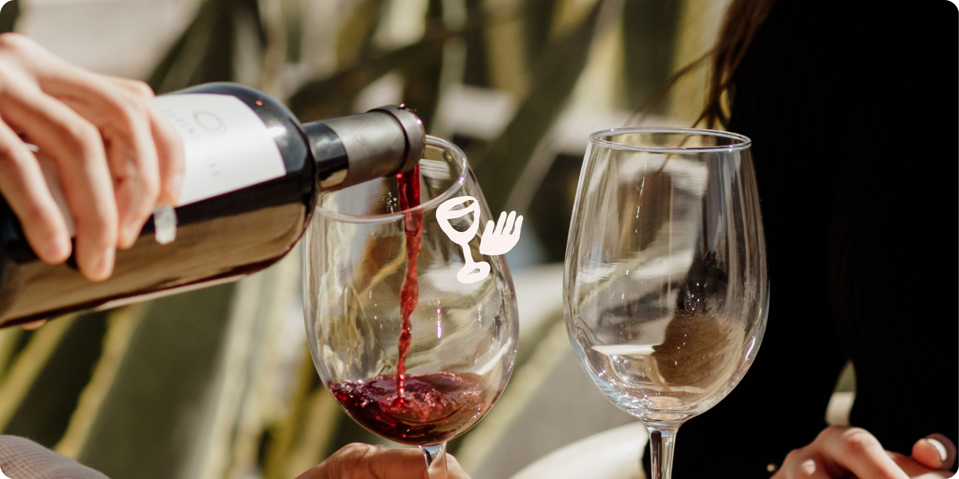 Wine being poured into a glass beside an empty wine glass at an outdoor table