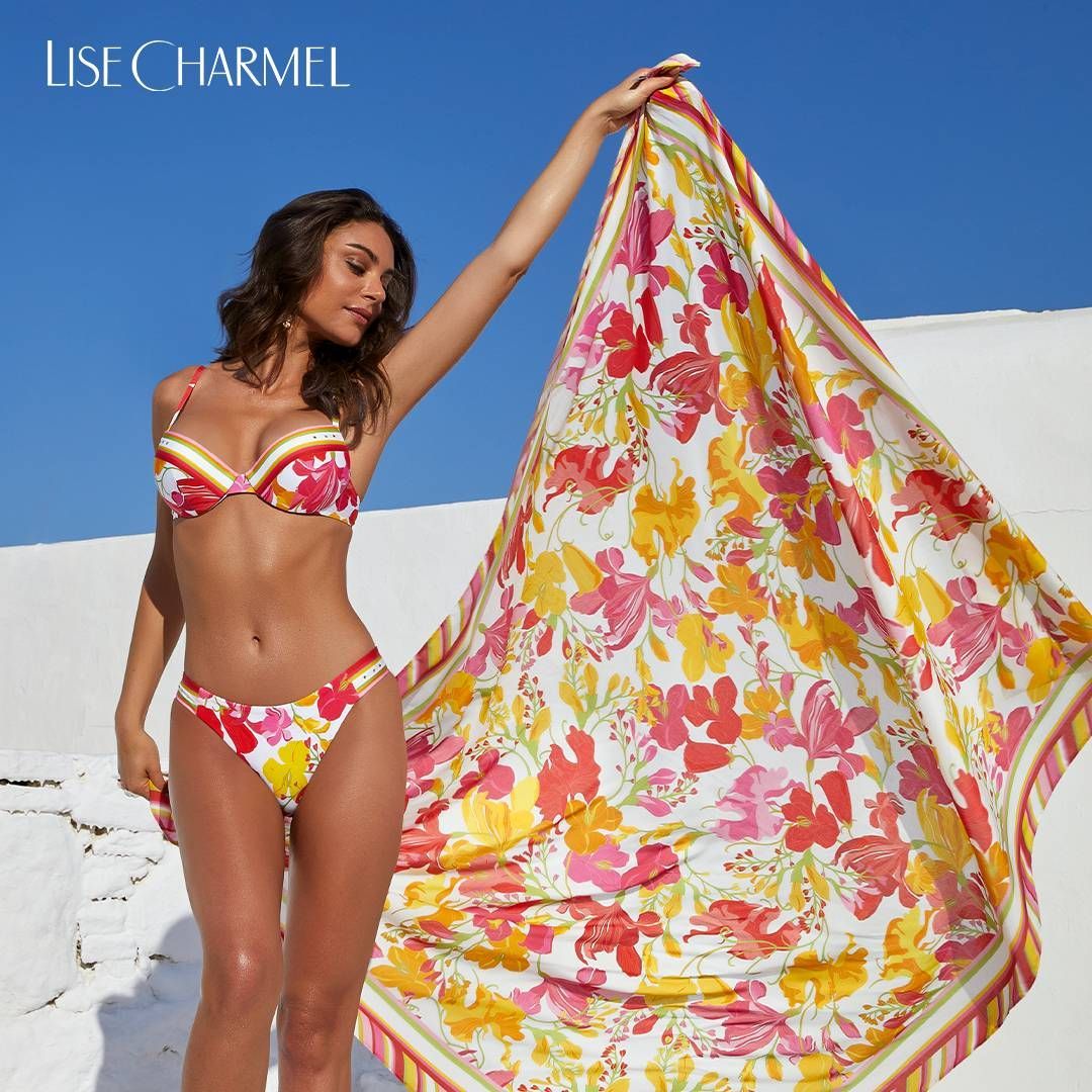 Femme en bikini fleuri tenant une écharpe assortie sous un soleil radieux.