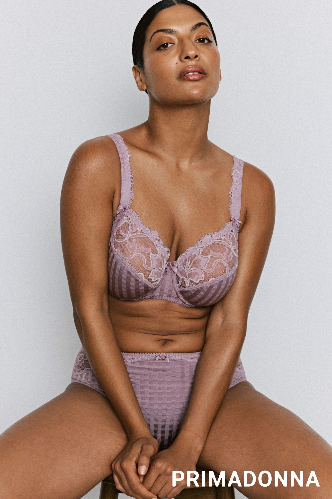 Femme assise, regardant vers le haut, portant un soutien-gorge en dentelle lilas et une culotte taille haute assortie.