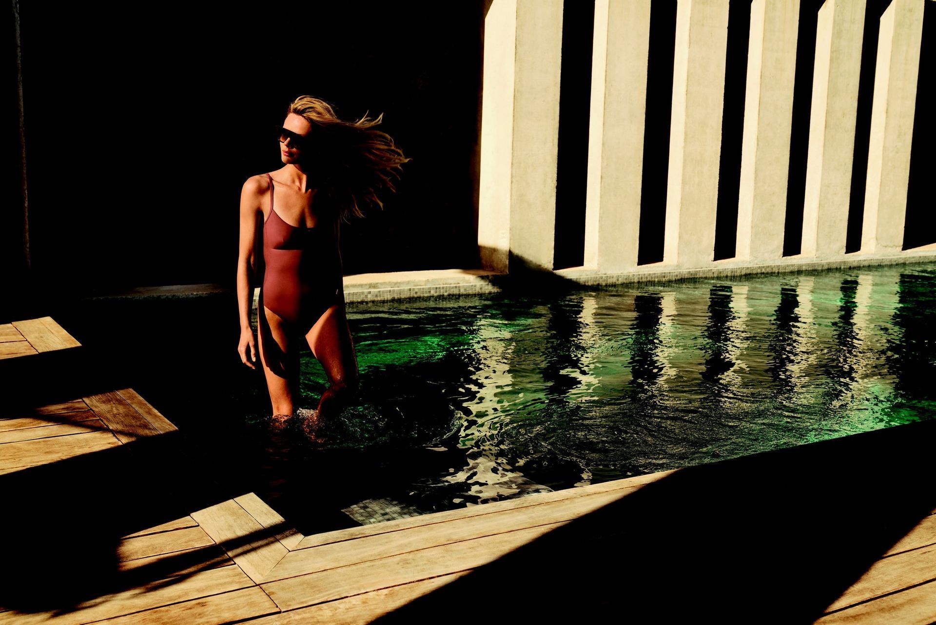 Une femme en maillot de bain rouge sort d'une piscine au soleil.