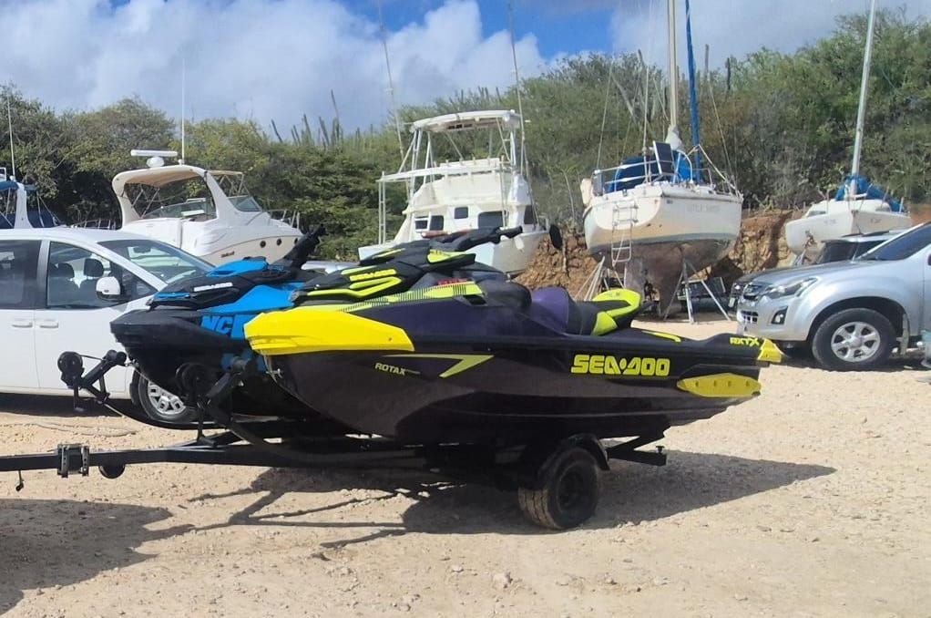 Een zwart-gele Sea-Doo waterscooter op een trailer op een parkeerplaats met boten en voertuigen op de achtergrond.